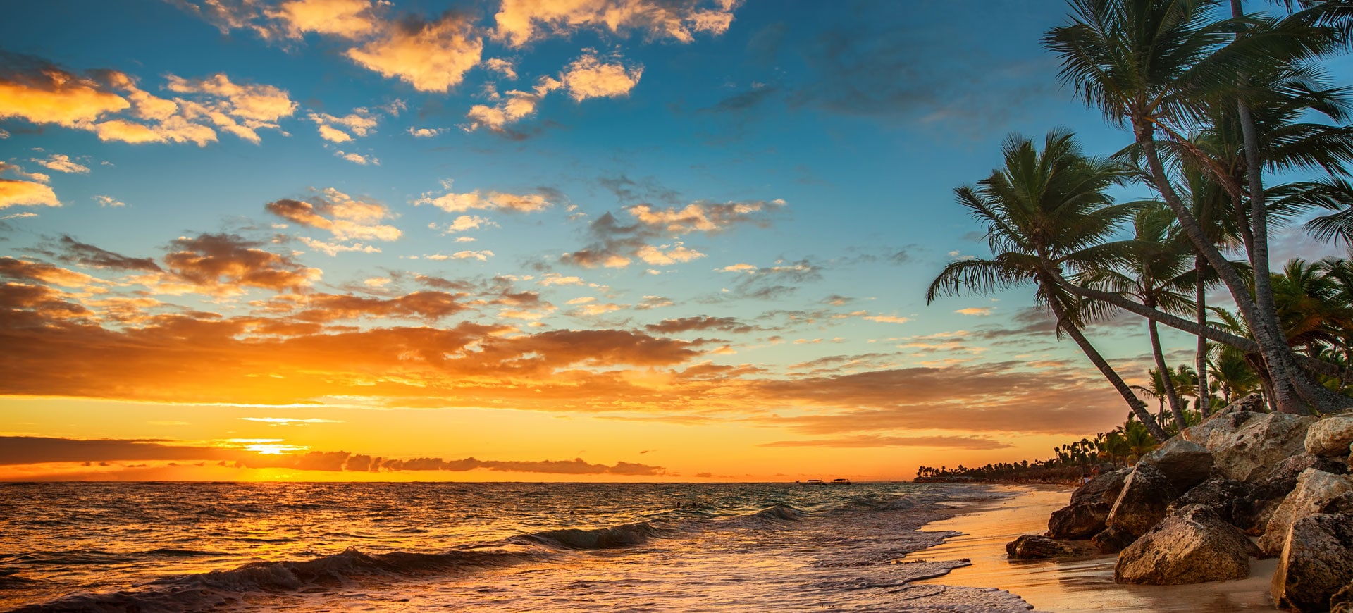 Tropical beach at sunset with palm trees over the water